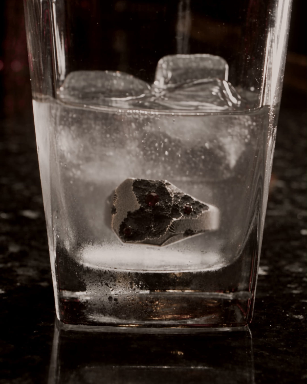 Silver signet ring at the bottom of a glass of iced water