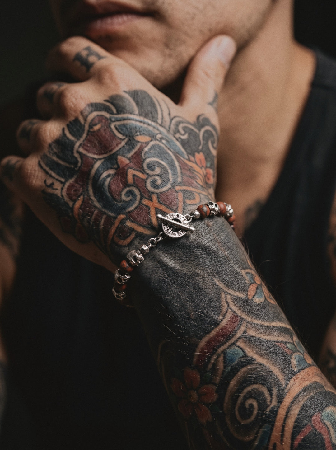 Raw I Bracelet with red brecciated beads, silver skulls and its toggle clasp, worn on a man's wrist covered in Japanese tattoos