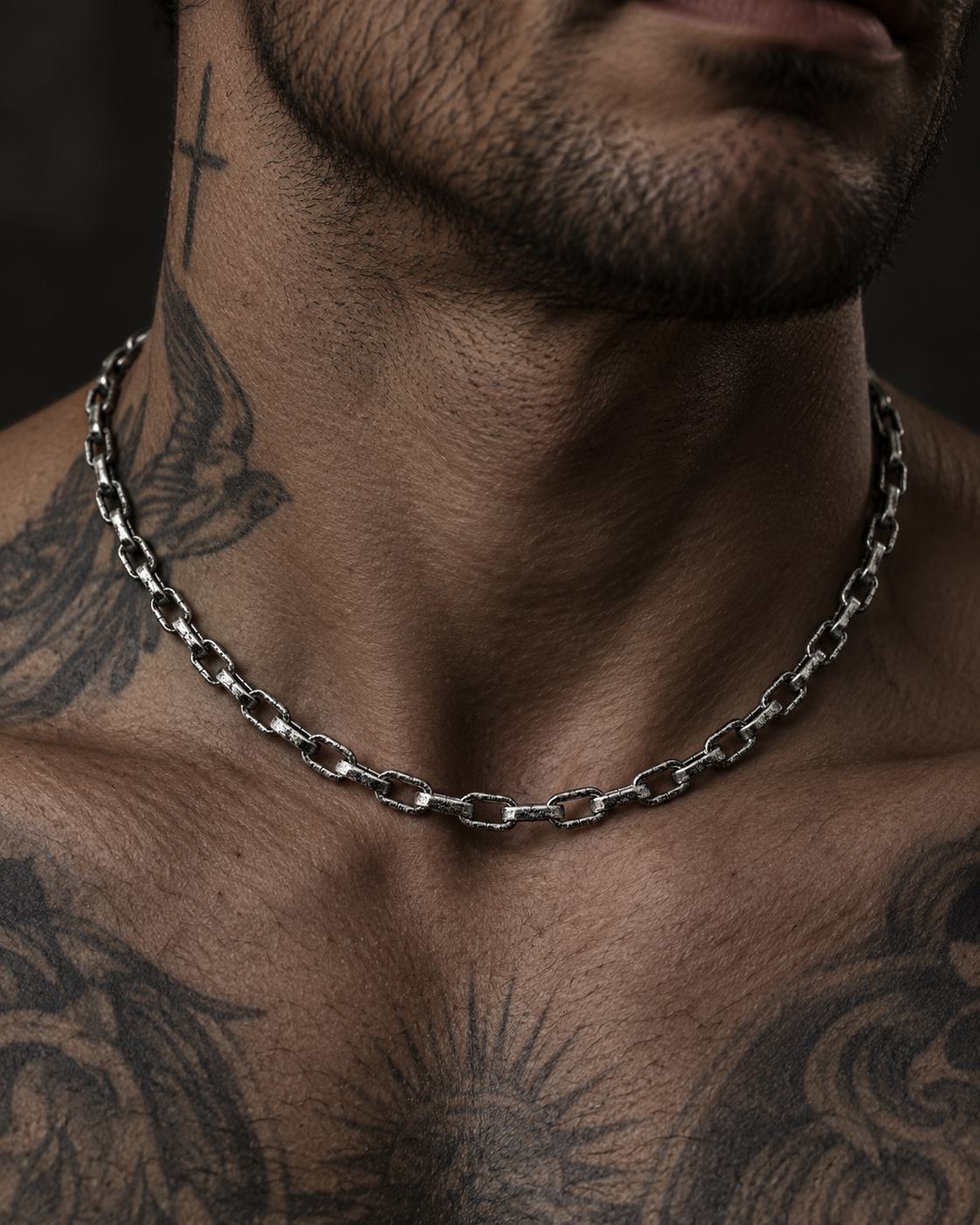 Raw I Necklace worn at the base of a man's throat, above a tattooed chest