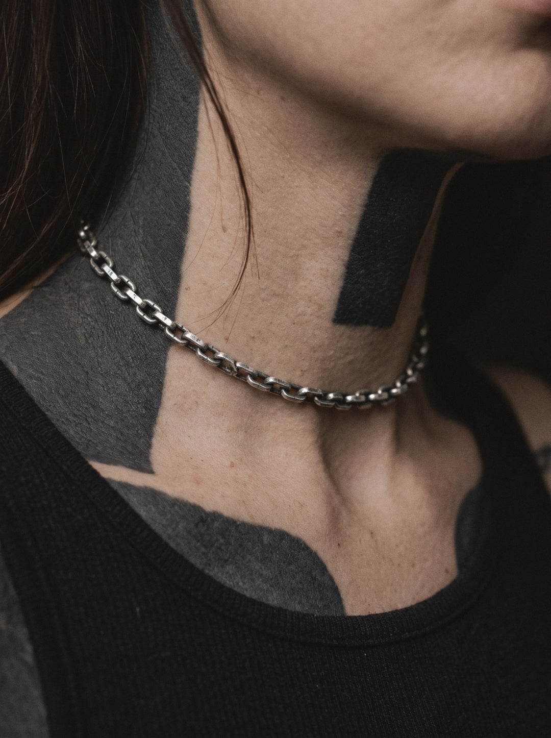 Raw I Necklace worn close at the base of a woman's neck, over blackwork tattoos, above a black tank top