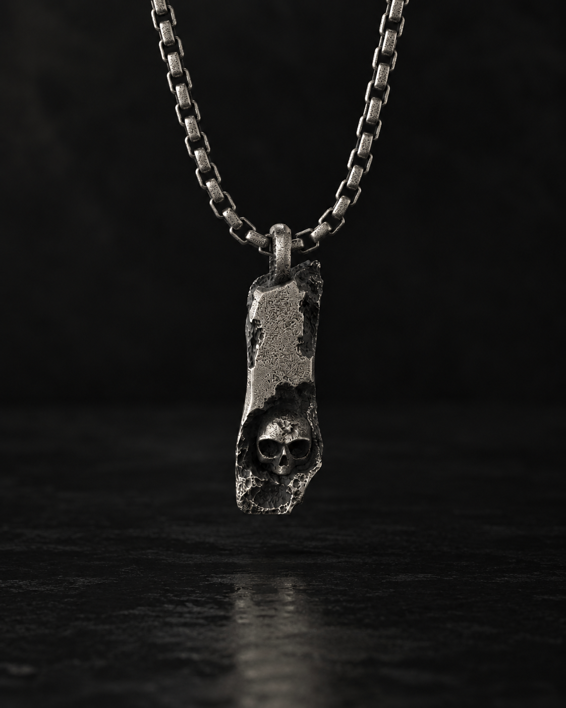 Raw I Pendant hanging from a box chain, cratered silver bar with a small skull at the base