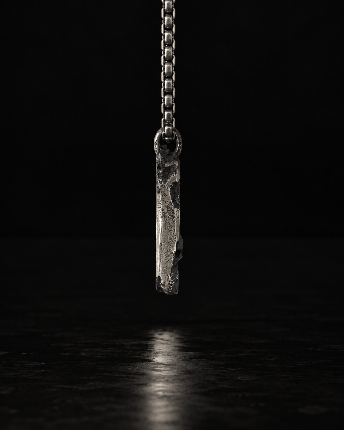 Raw I Pendant edge on in low light, the chain running up out of frame