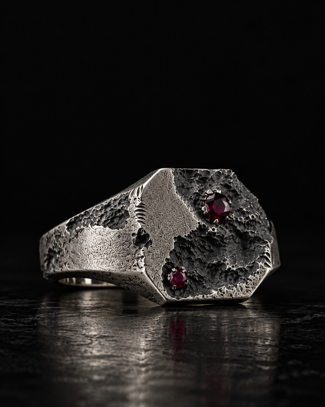 Raw I Ring at an angle on black, two red stones in the cratered top and mould marks on the shoulder