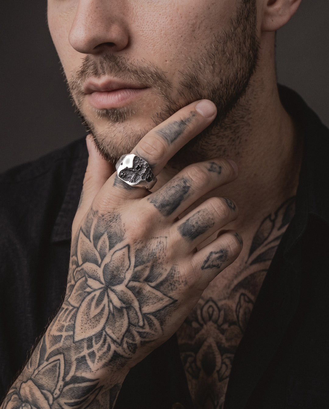 Raw I Ring with Black Spinel stones worn by a man on his index finger, his heavily tattooed hand at his chin