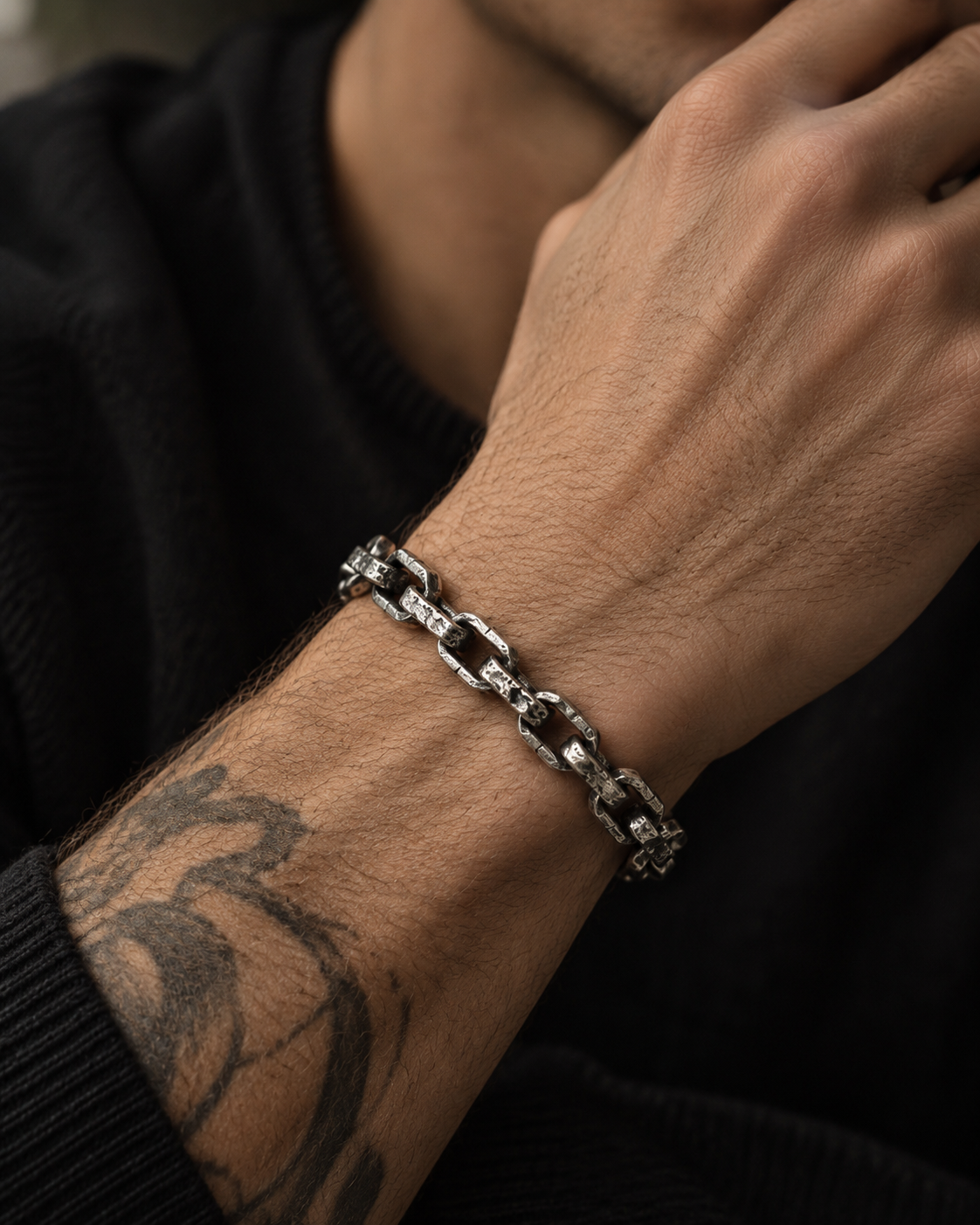 Raw II Bracelet on a man's tattooed wrist, hand raised to his chin, black knit sleeve
