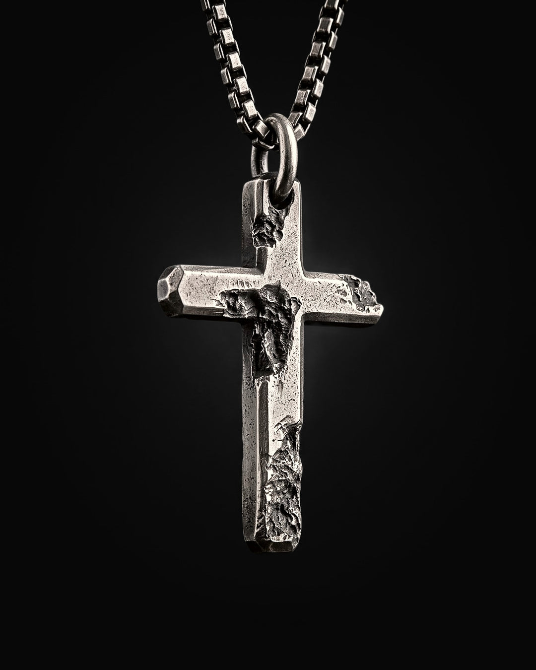 Raw II Pendant at an angle on its box chain, the bevelled ends and the deep craters across the arms of the silver cross