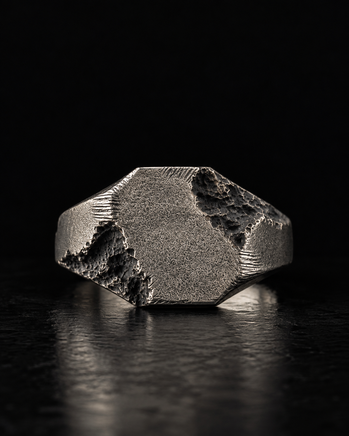 Raw II Ring seen face on, worn-down signet plate with rough broken edges on a dark reflective surface