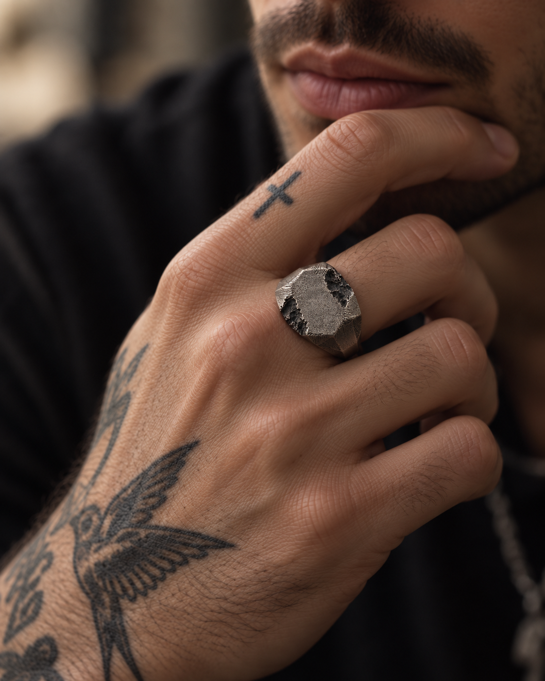 Raw II Ring on a tattooed man's hand, signet plate turned to the camera, hand resting at his chin