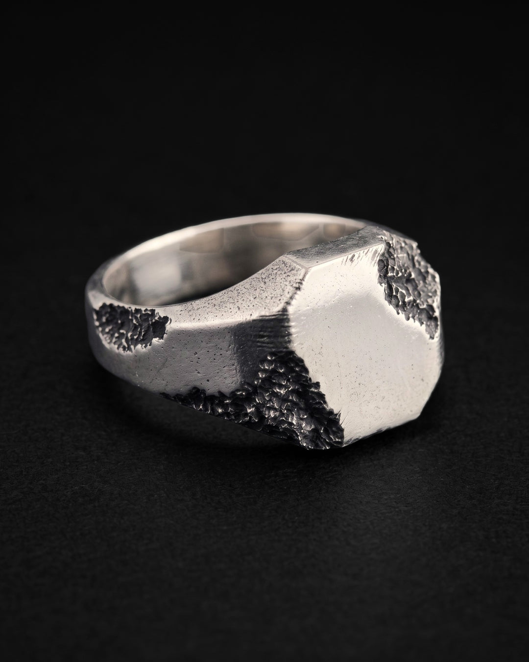 Raw II Ring turned three quarters on black, the satin signet plate with cratered corners and craters along the shank