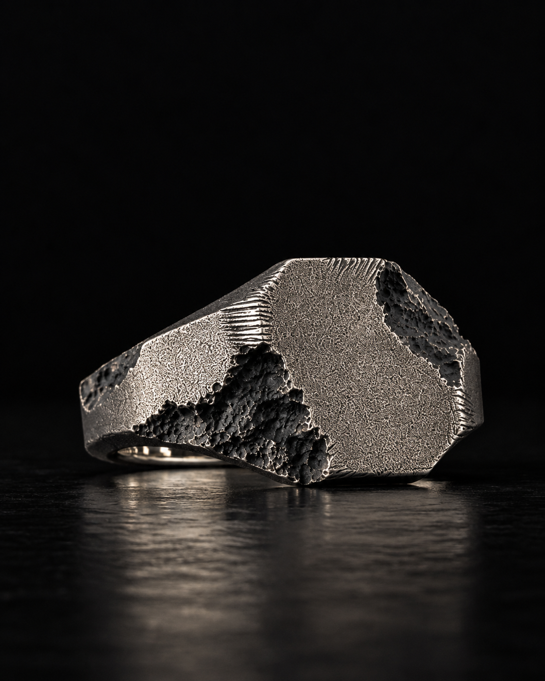 Raw II Ring turned three quarters, signet plate and faceted shank against a dark background
