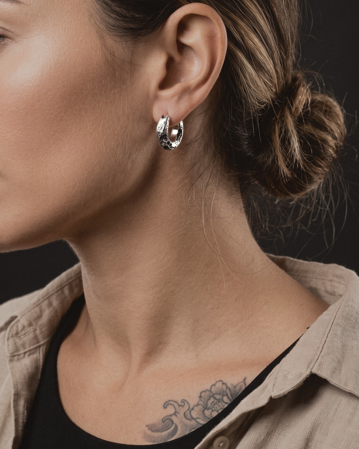 Raw III Earring worn on a woman's left ear, a small cratered silver hoop below a low bun
