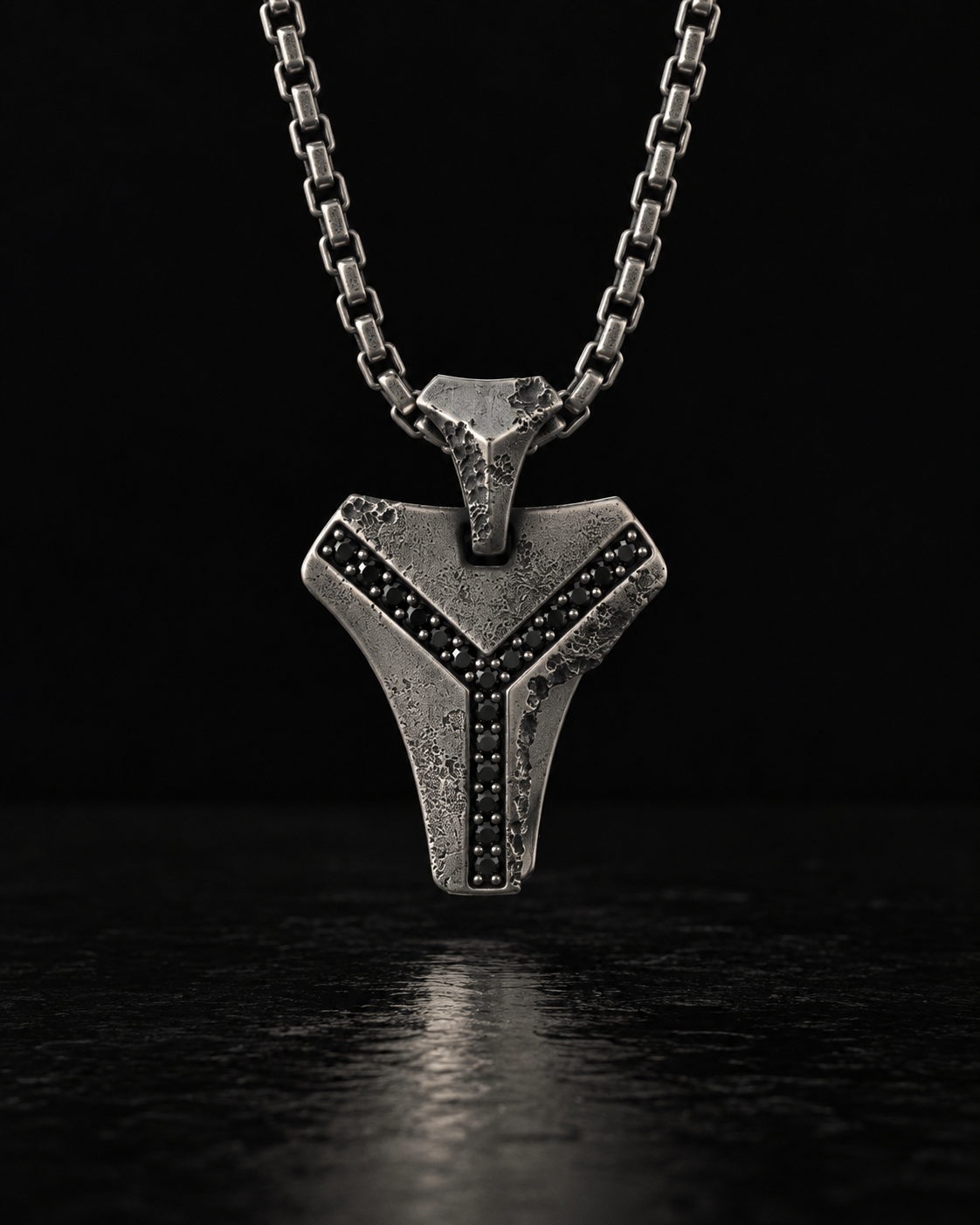 Raw III Pendant hanging from a box chain, black stones set along the Y channel, on a black surface