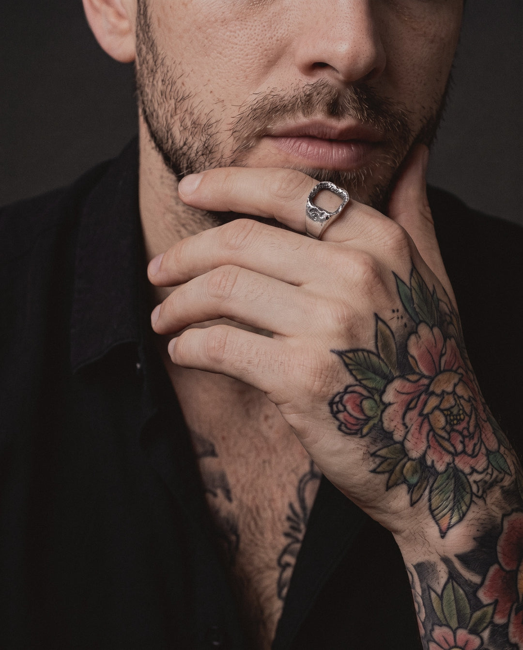 Raw III Ring worn by a man on his index finger, his hand at his chin, neo-traditional colour tattoos on his hand and arm