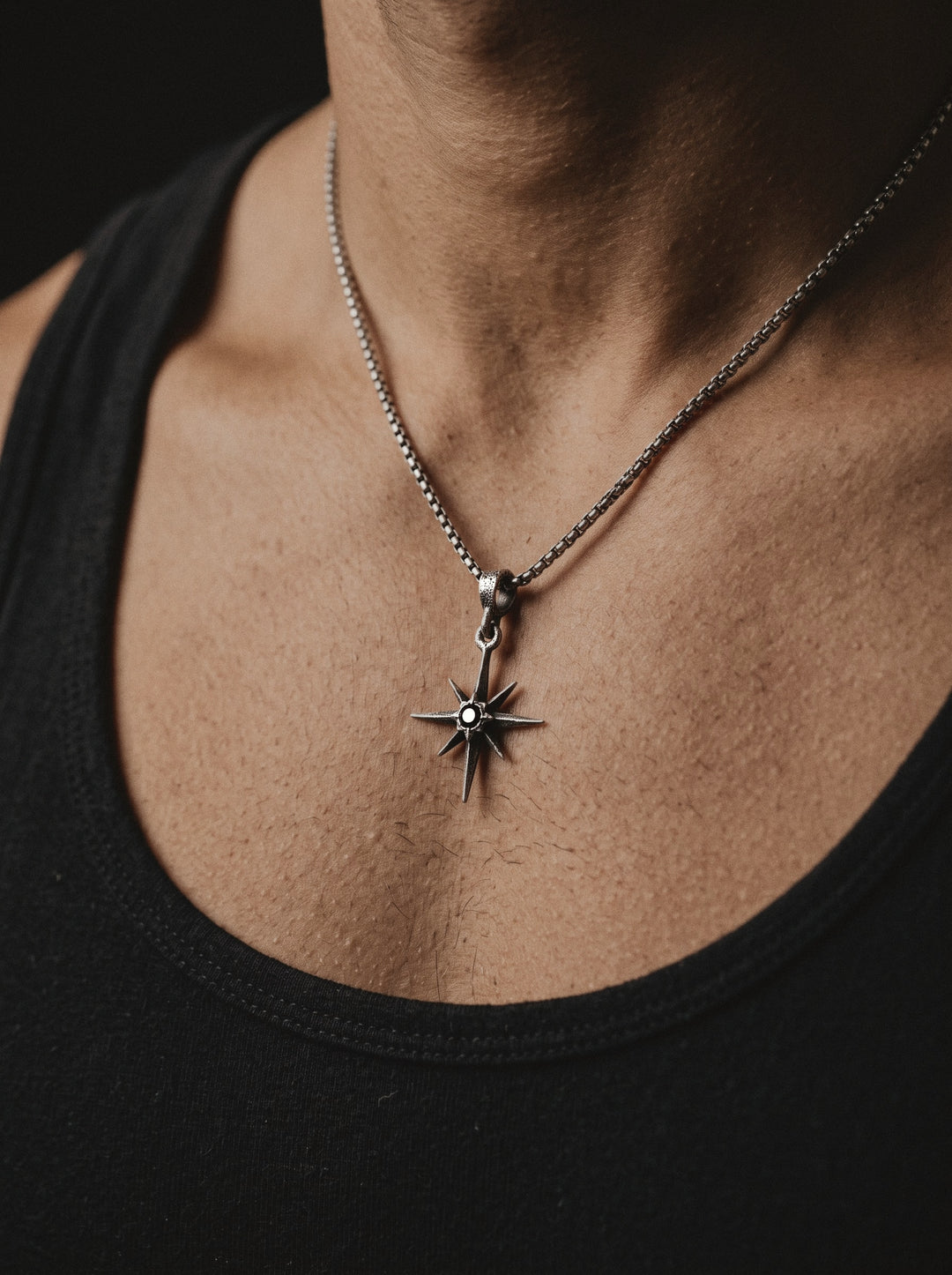 Raw IV Pendant on a box chain, the small star worn on a man's chest above a black tank top