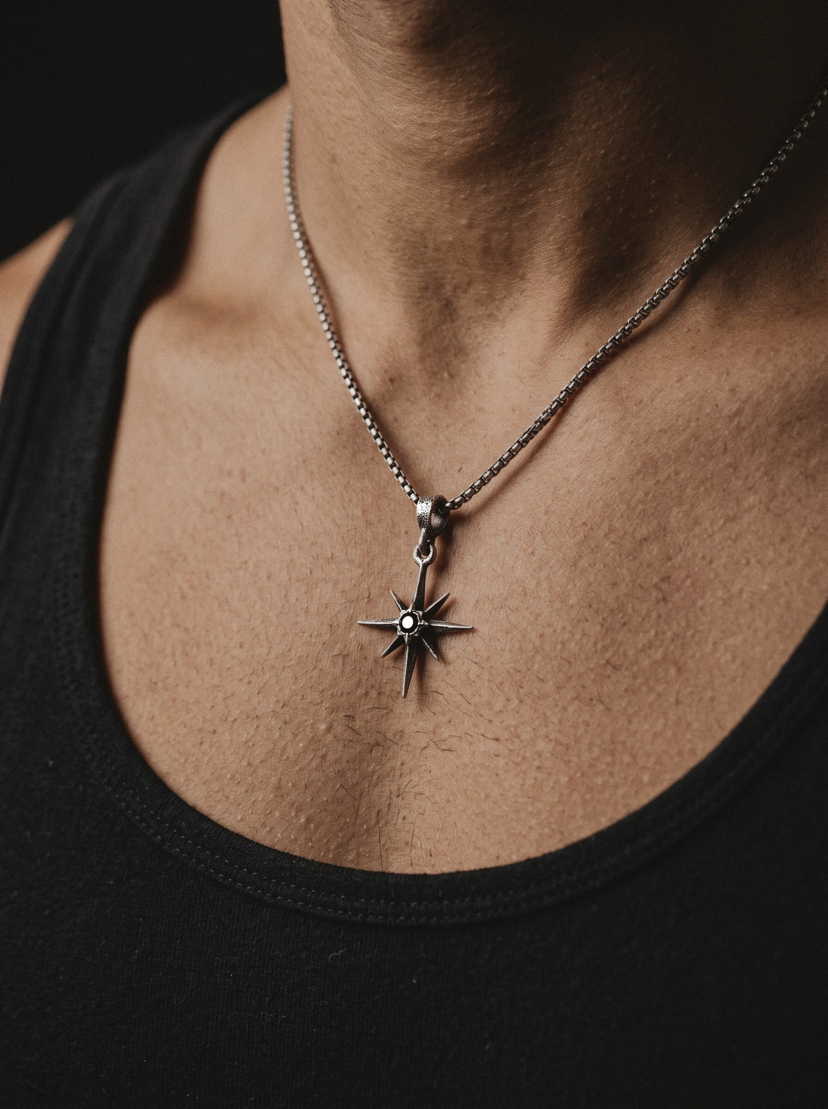 Raw IV Pendant on a box chain, the small star worn on a man's chest above a black tank top