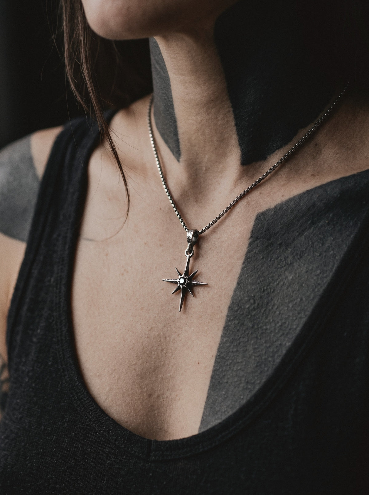 Raw IV Pendant on a box chain, the small star worn on a woman's chest with blackwork tattoos, above a black tank top