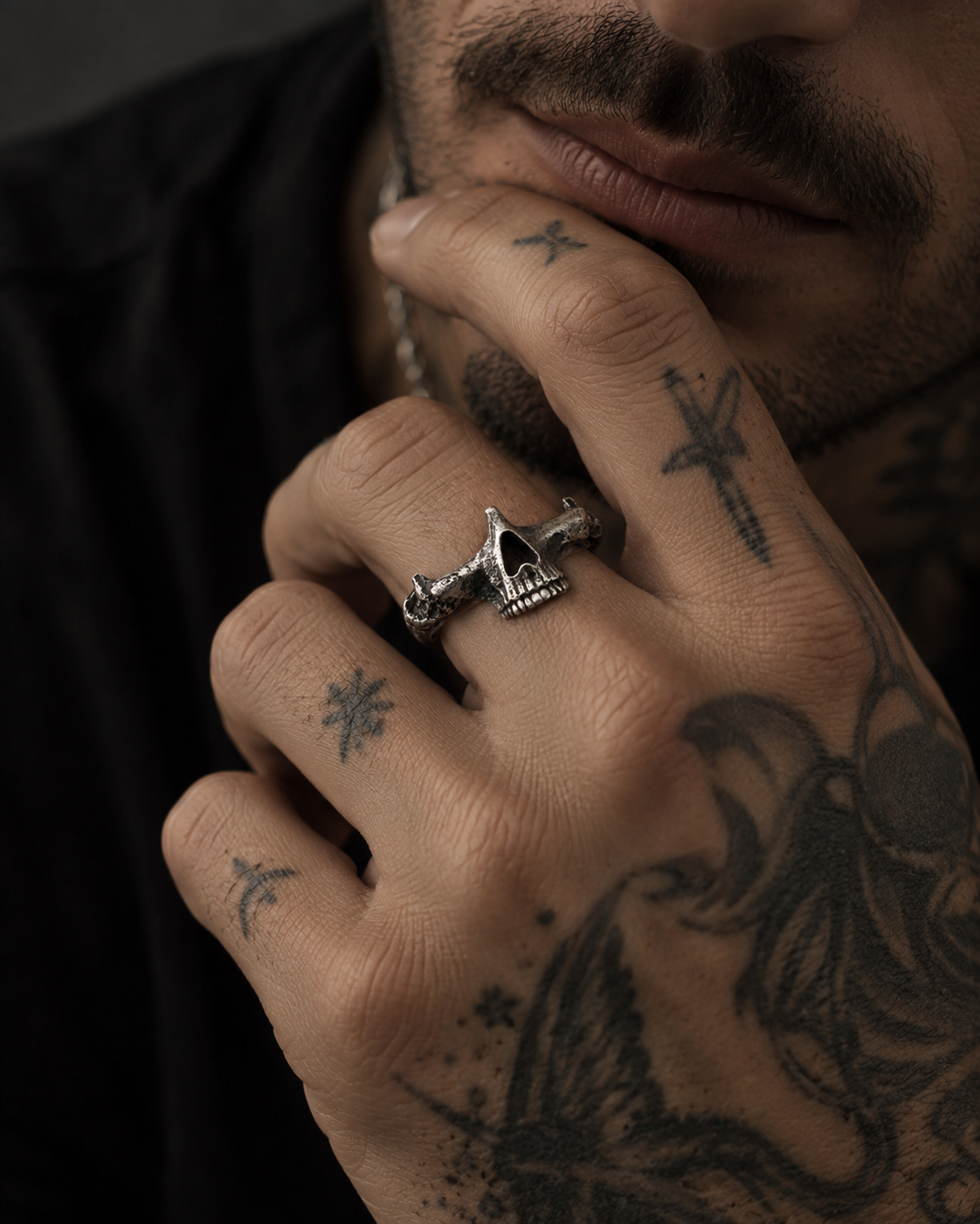Raw IV Ring on the middle finger of a tattooed hand held to a bearded jaw