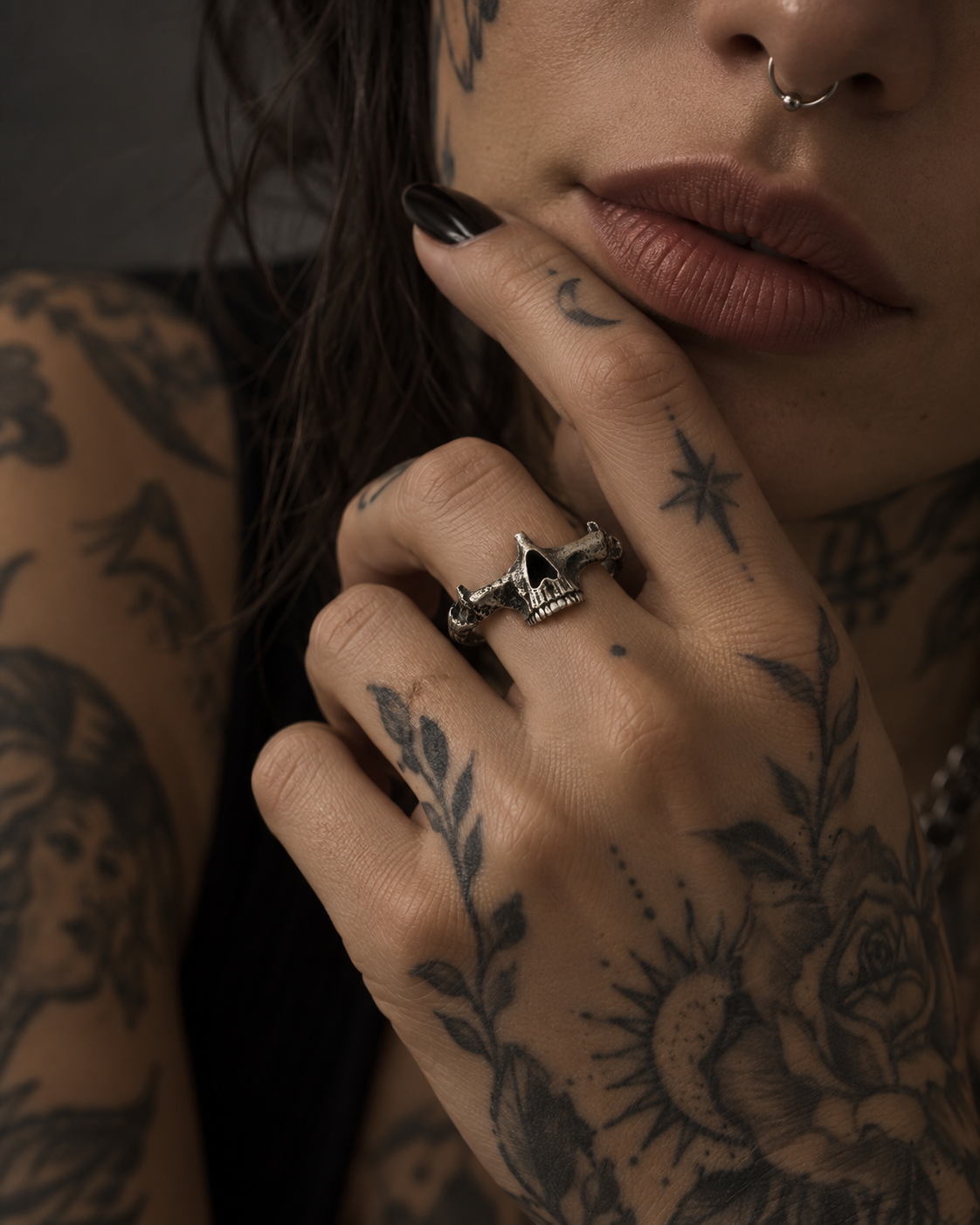 Raw IV Ring on the middle finger of a tattooed hand with dark nails