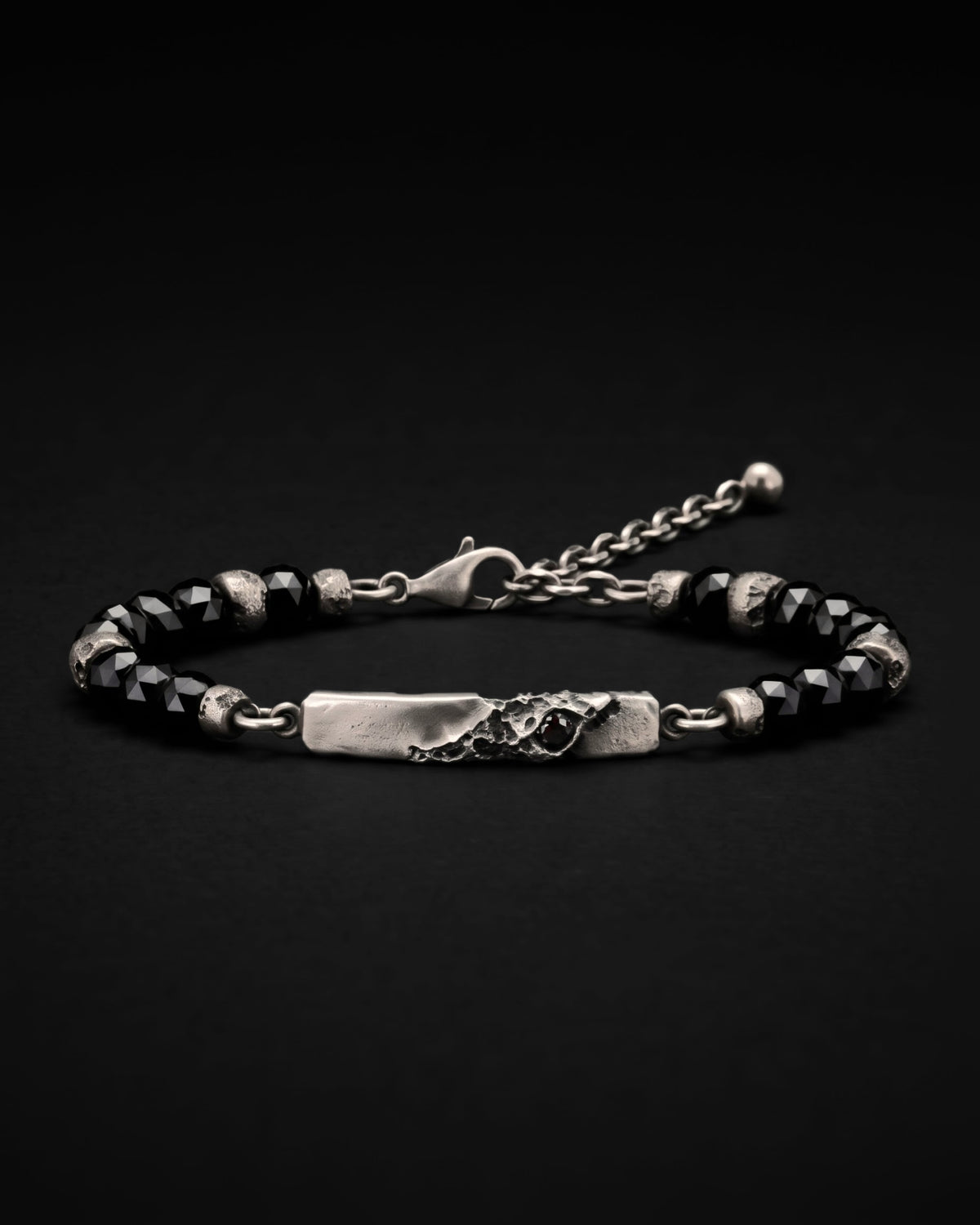 Raw V Bracelet, a cratered silver bar set with a black spinel between faceted black spinel beads and cratered silver spacers, against black