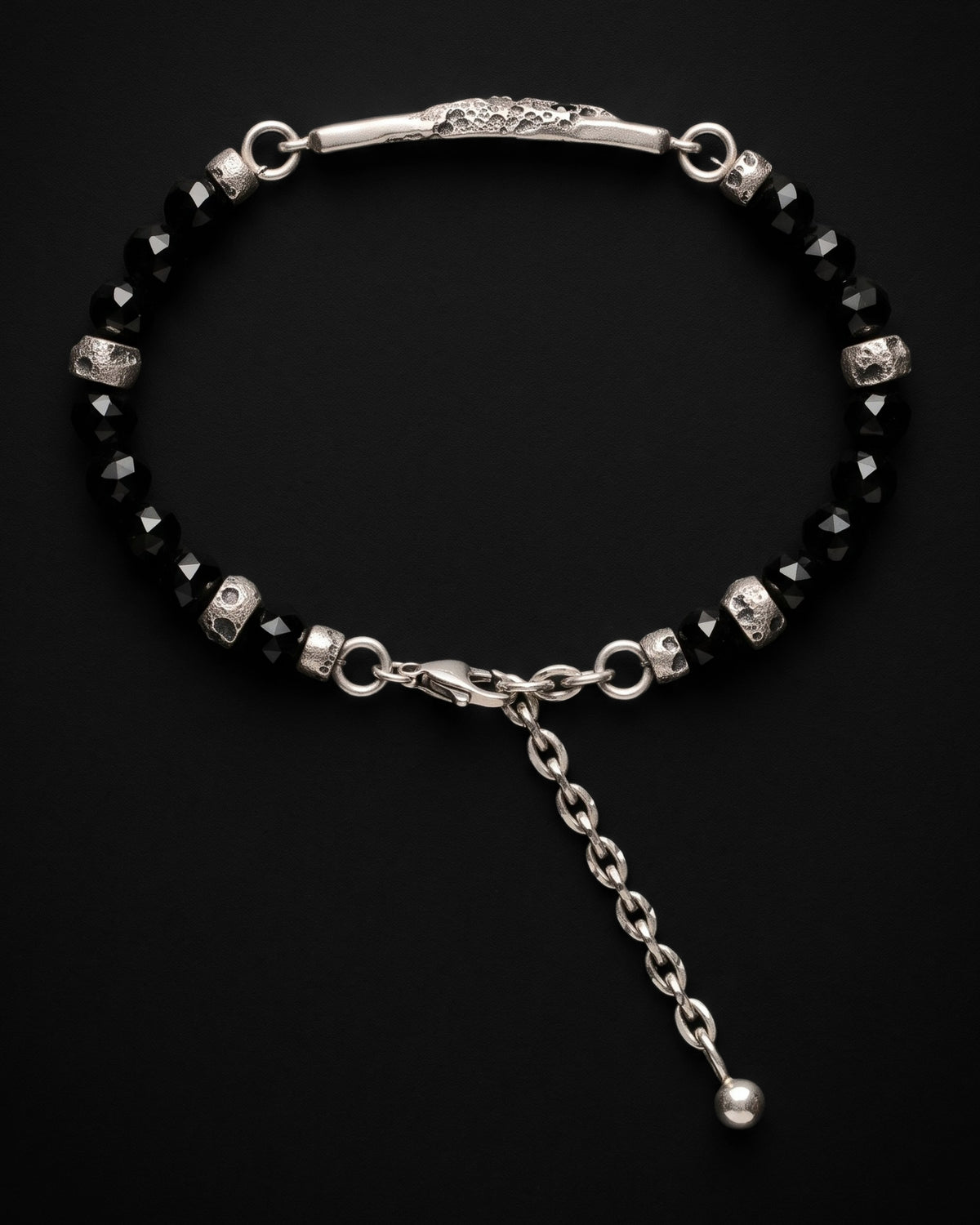 Raw V Bracelet visto dall'alto, perle di spinello nero, distanziatori con crateri e la catenella di estensione con la sua pallina