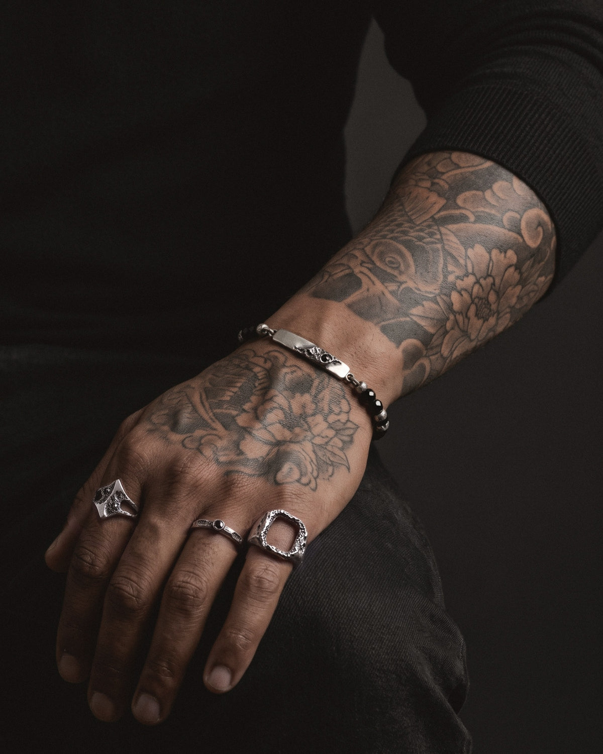 Raw V Bracelet with black spinel beads worn on a tattooed wrist, the cratered silver bar on top, black knit sleeve