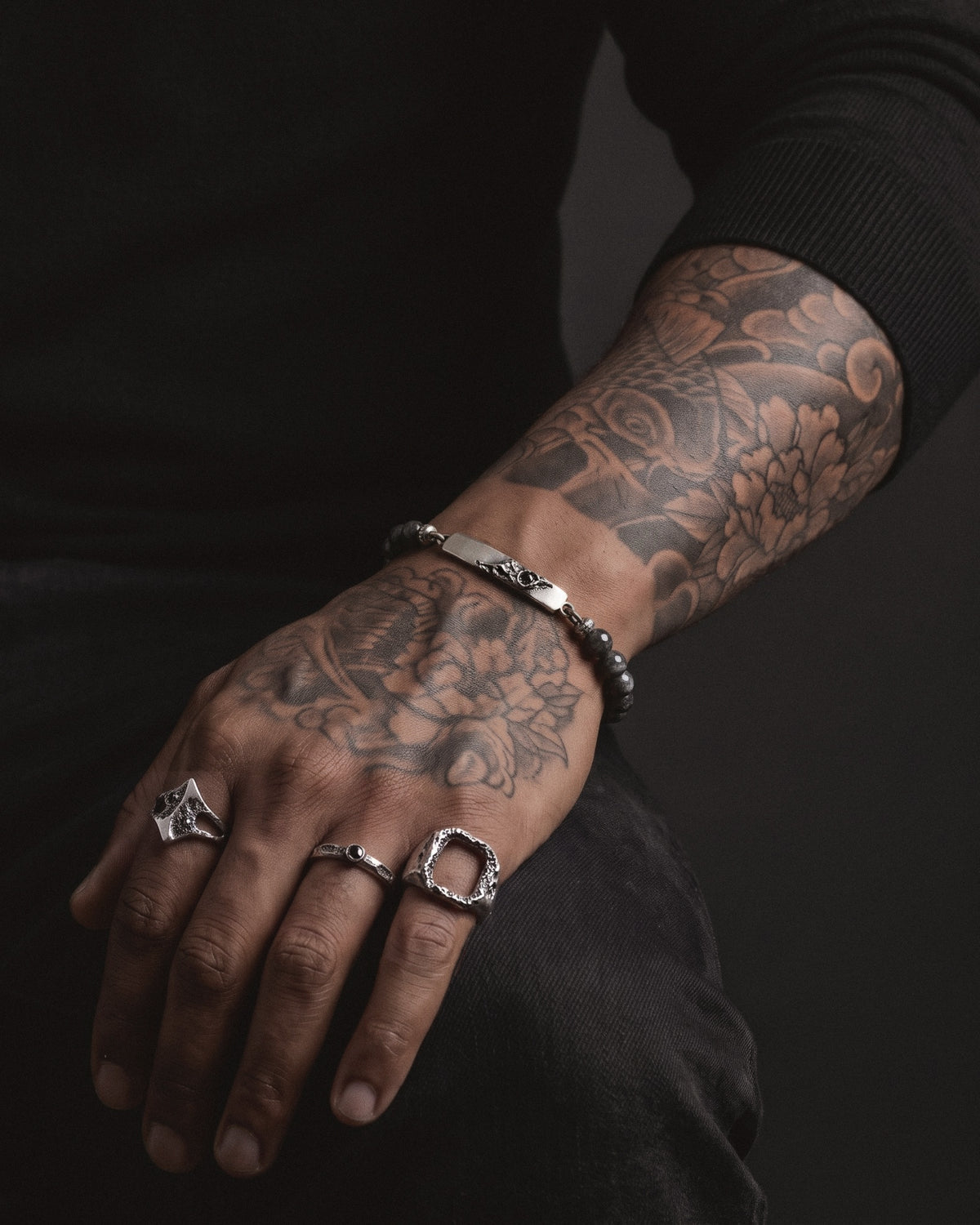 Raw V Bracelet with labradorite beads worn on a tattooed wrist, the cratered silver bar with its black spinel on top
