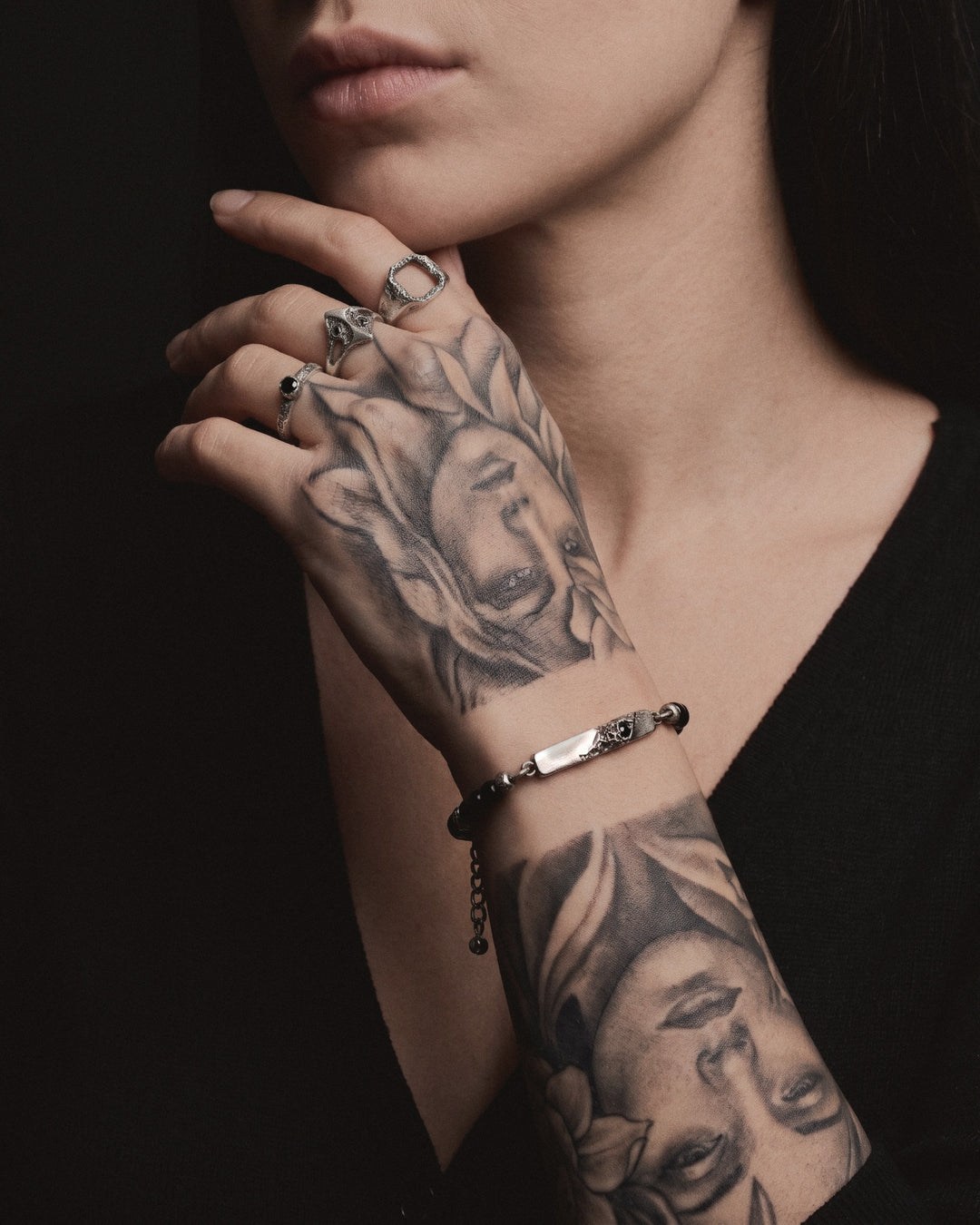 Raw V Bracelet with black spinel beads on a woman's tattooed wrist, her hand at her chin stacked with Raw rings