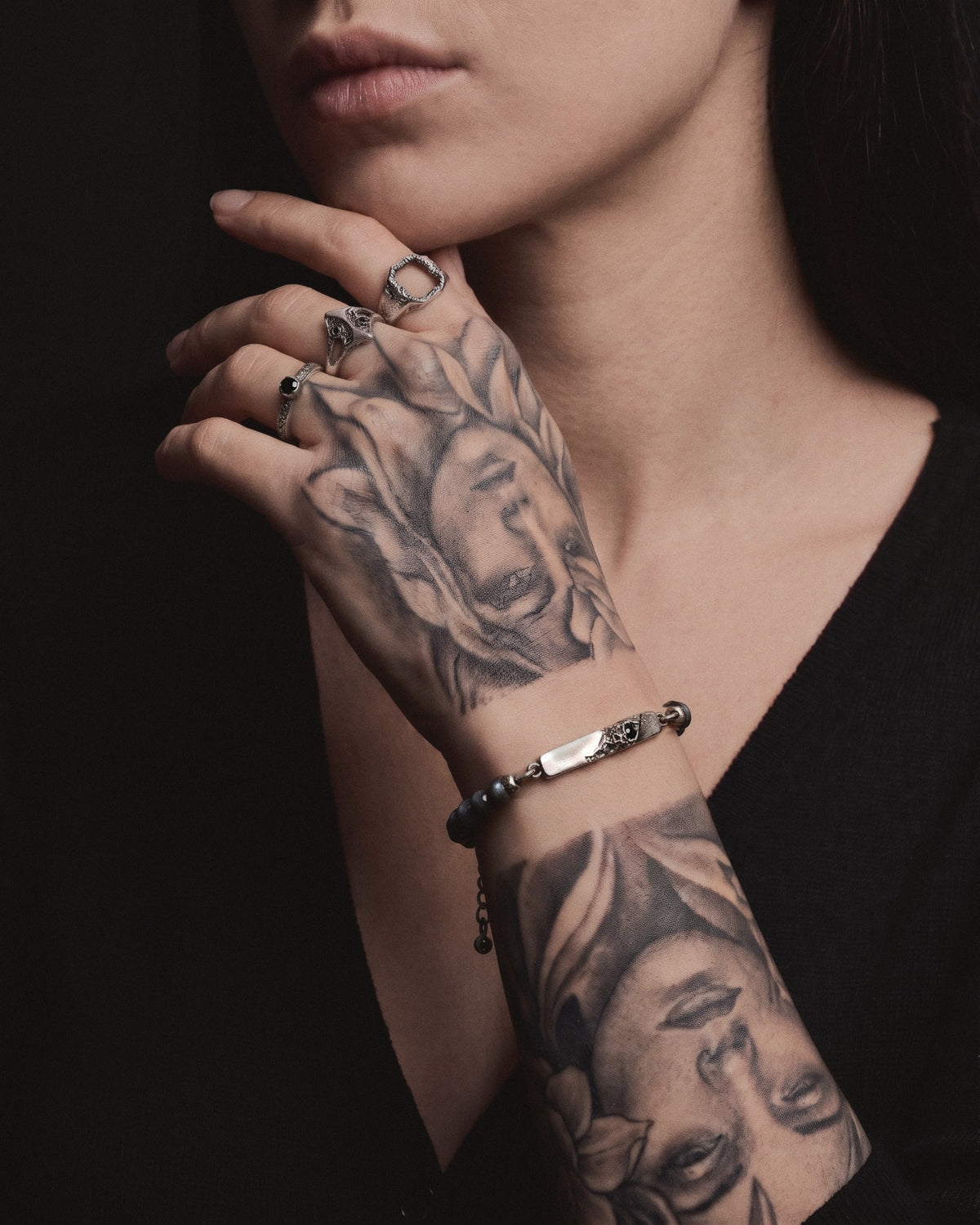 Raw V Bracelet with labradorite beads on a woman's tattooed wrist, her hand at her chin stacked with Raw rings
