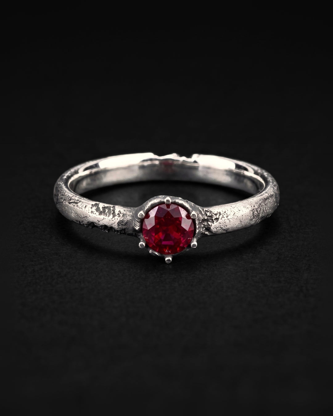 Raw V Ring face on, the round ruby in its six prongs with patches of pitting on the band