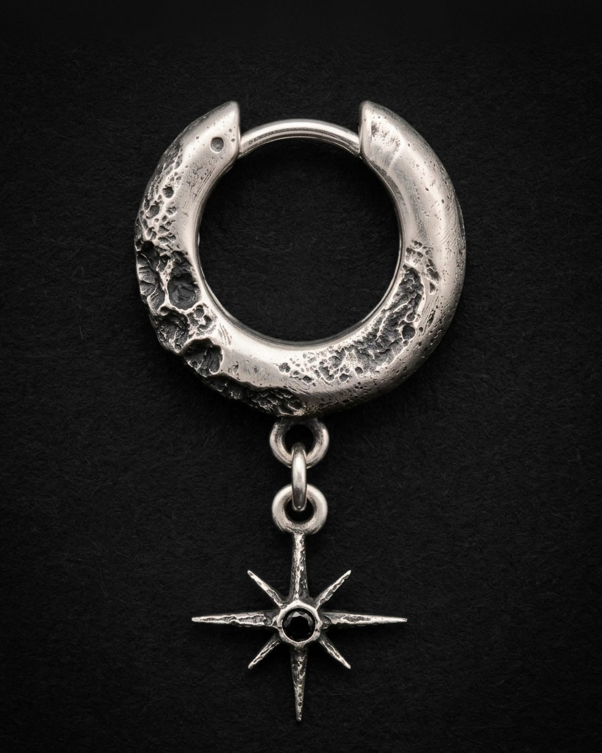 Raw VI Earring from the front, the cratered silver hoop and the star with its black stone hanging straight from two rings