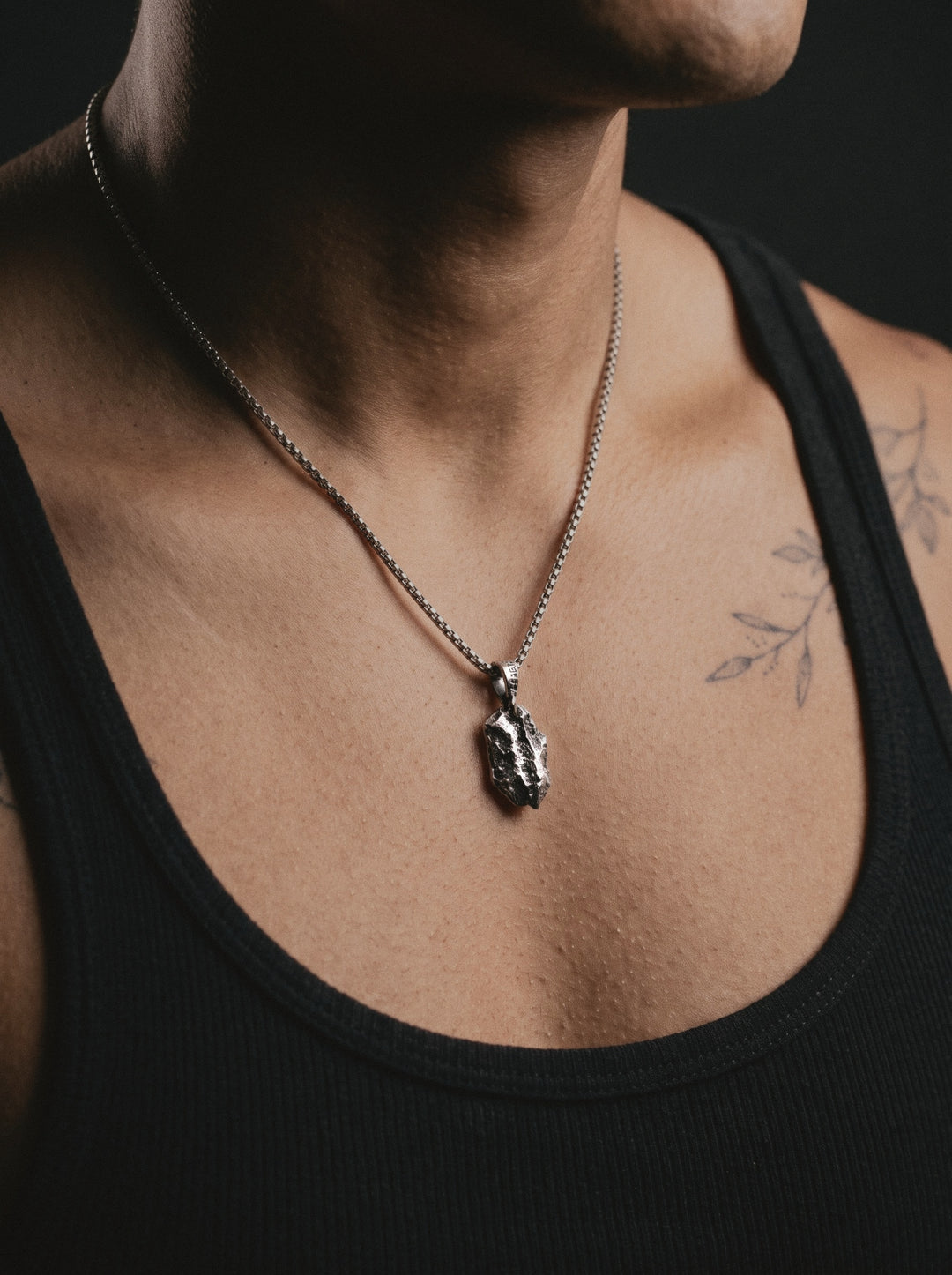 Raw VI Pendant on a box chain, worn on a man's chest above a black ribbed tank top