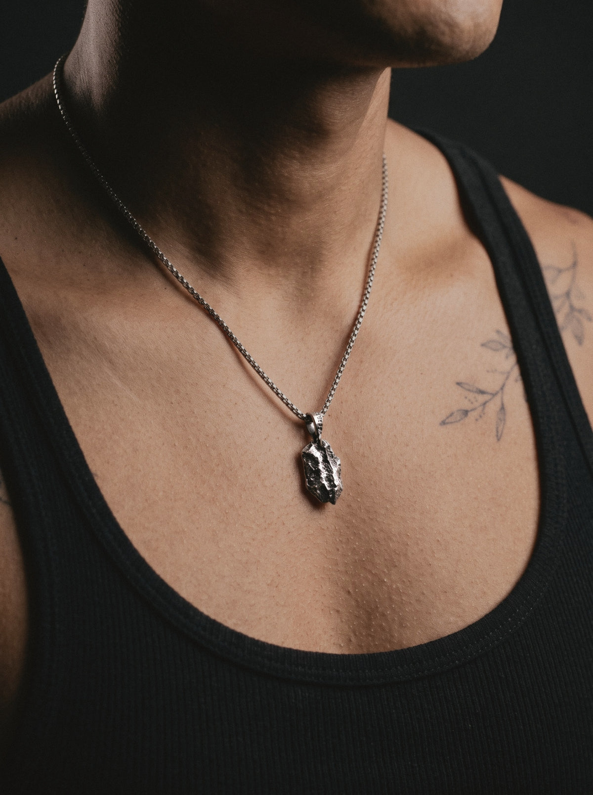 Raw VI Pendant on a box chain, worn on a man's chest above a black ribbed tank top