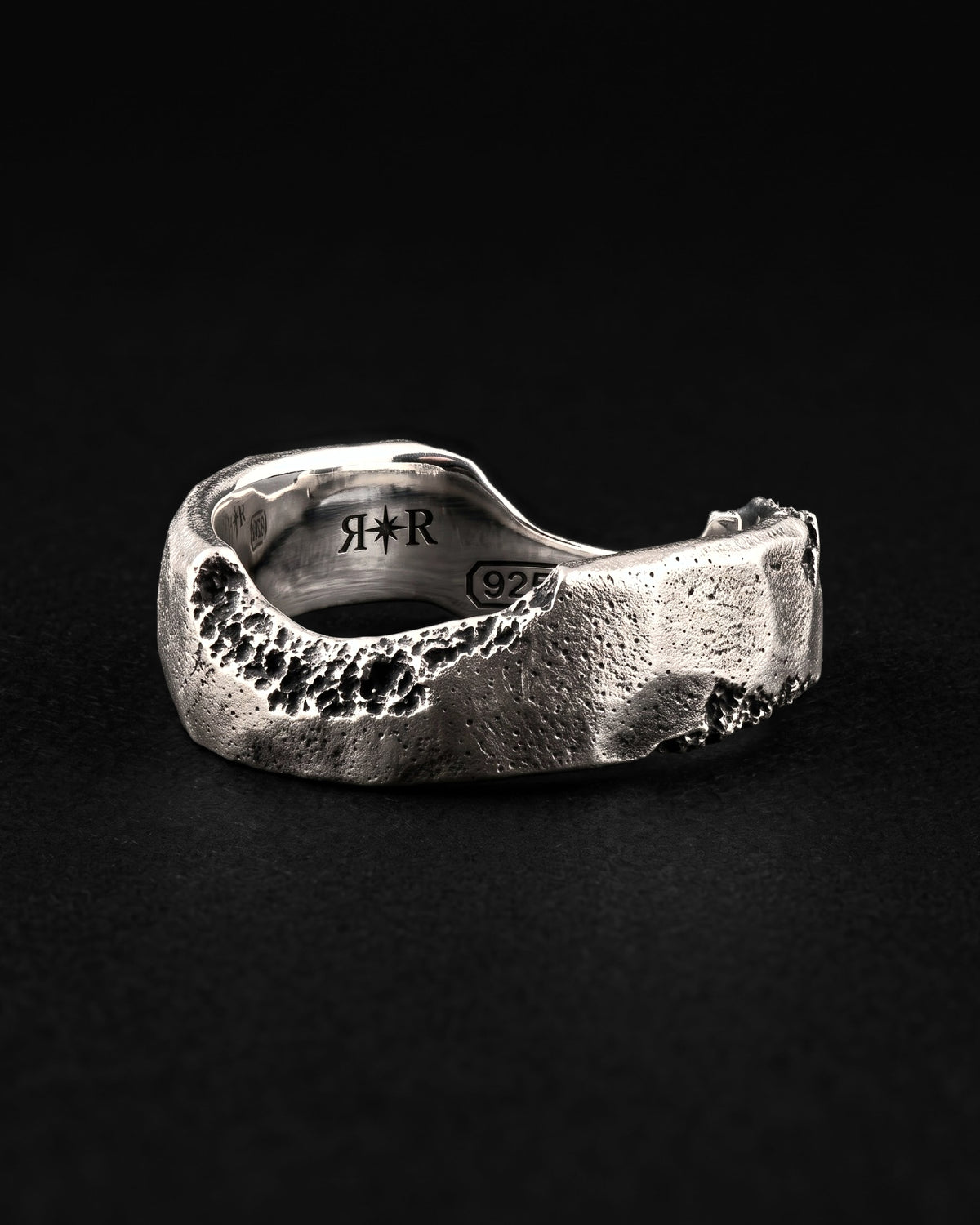 Raw VI Ring at an angle on black, the wavy band with dark craters and the RR star hallmark and 925 laser engraved inside