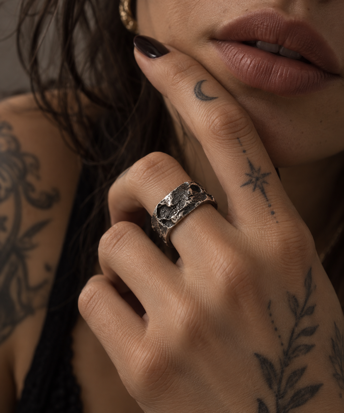 Raw VI Ring on a tattooed hand held to the face, wide cratered band