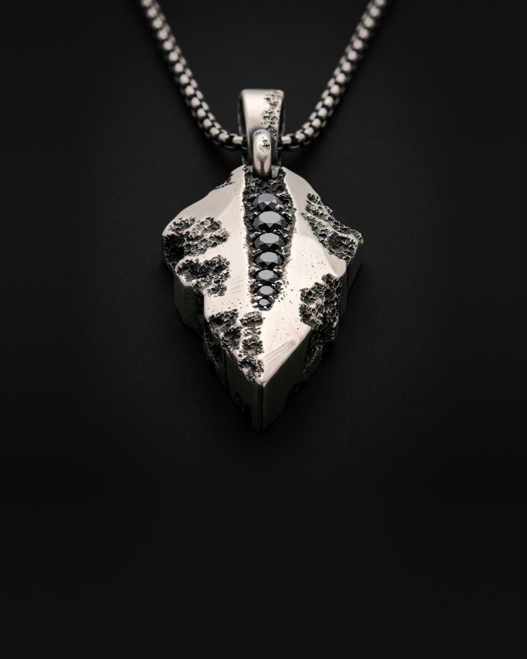 Raw VIII Pendant seen from a low angle, the cratered arrowhead and its line of black stones receding towards the bail