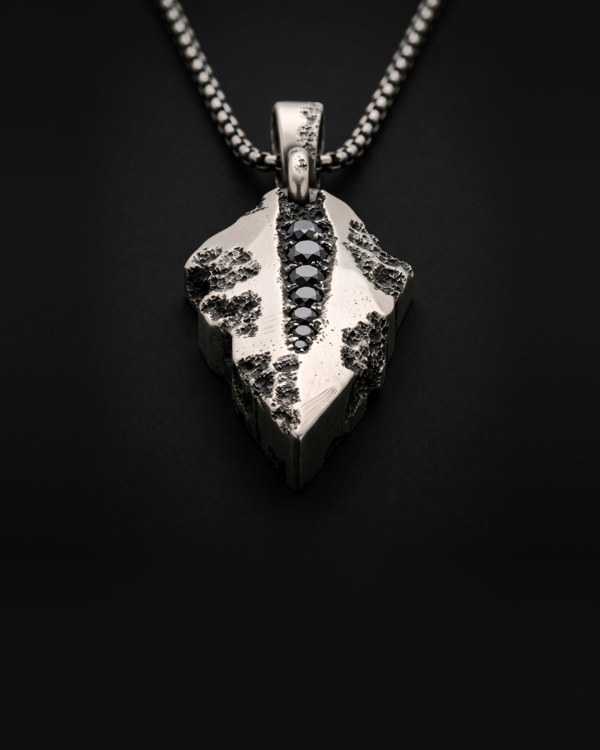 Raw VIII Pendant seen from a low angle, the cratered arrowhead and its line of black stones receding towards the bail