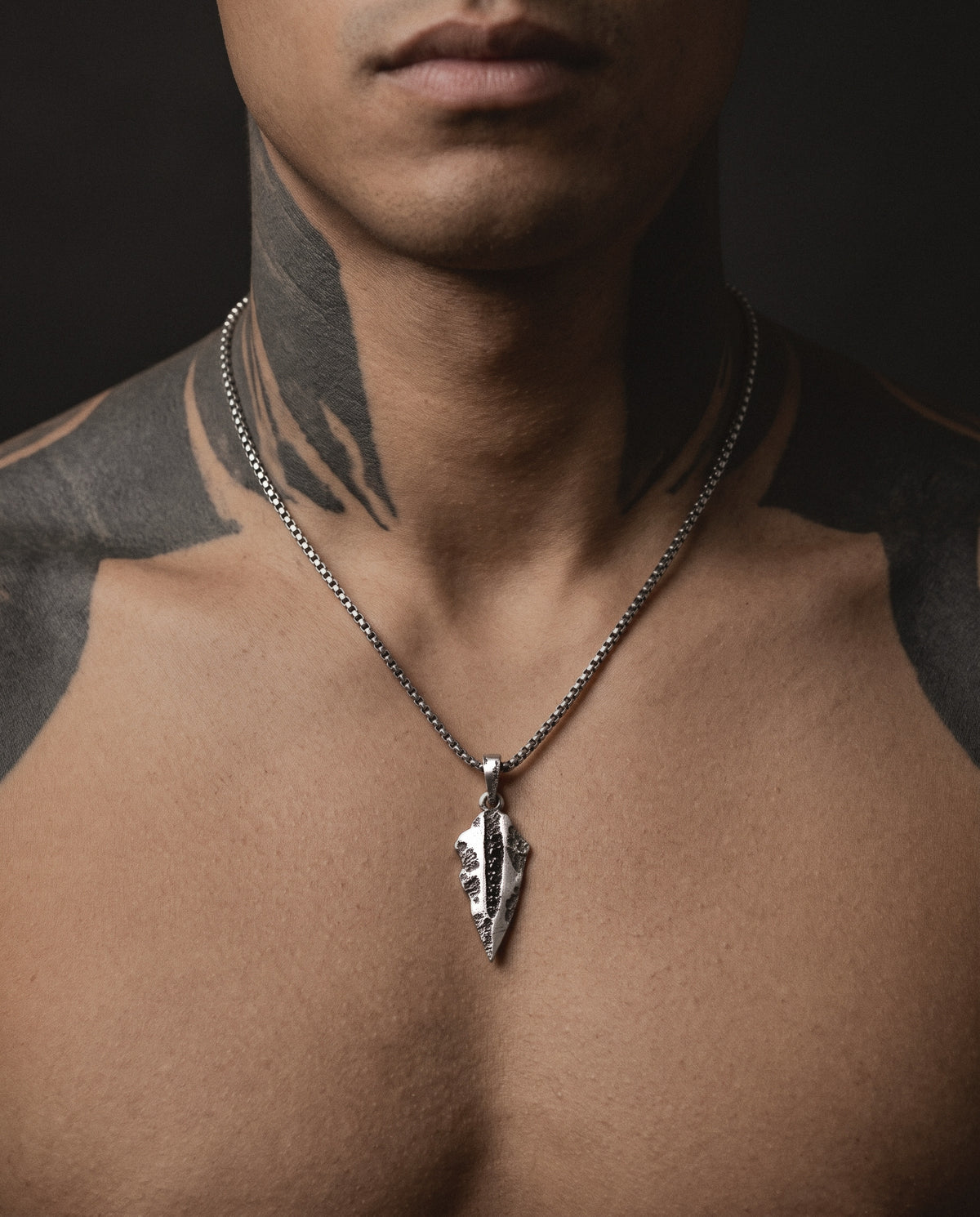 Raw VIII Pendant on a box chain, worn on a tattooed man's bare chest