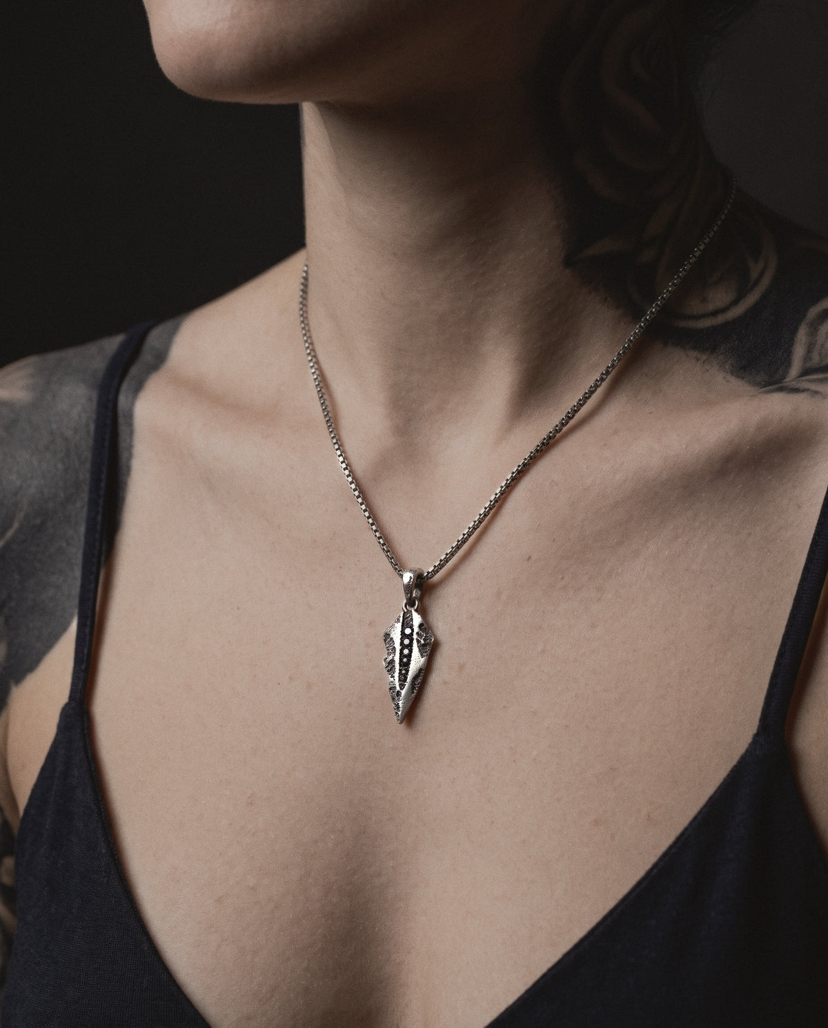 Raw VIII Pendant on a box chain, worn on a tattooed woman's chest above a black strappy top