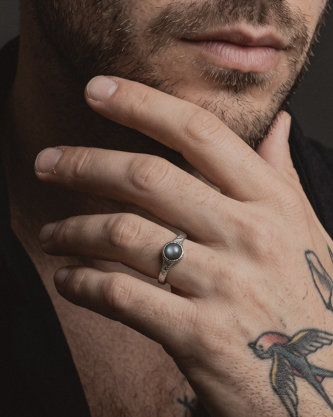 Raw VIII Ring with labradorite worn by a man, his hand at his chin, American traditional tattoos on his hand and forearm