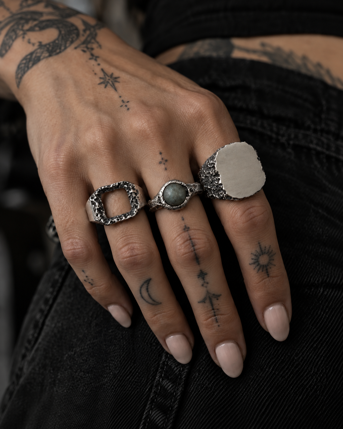 Raw VIII Ring with labradorite worn on a woman's tattooed hand, next to an open square ring and a signet