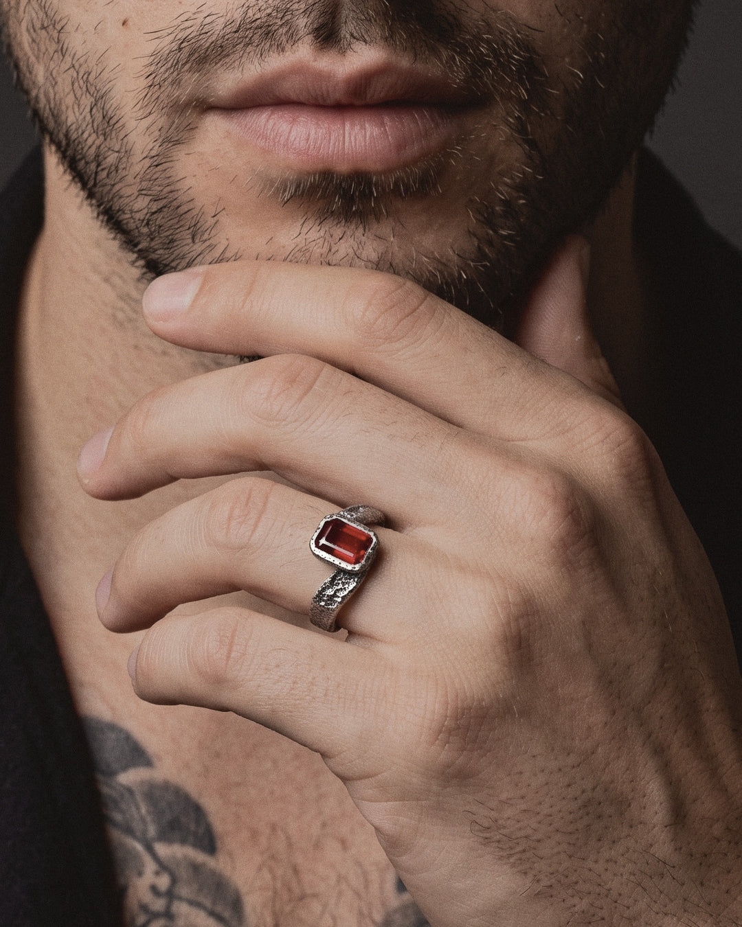 Raw X Ring worn by a man, his hand at his chin, Japanese style tattoos on his chest and forearm