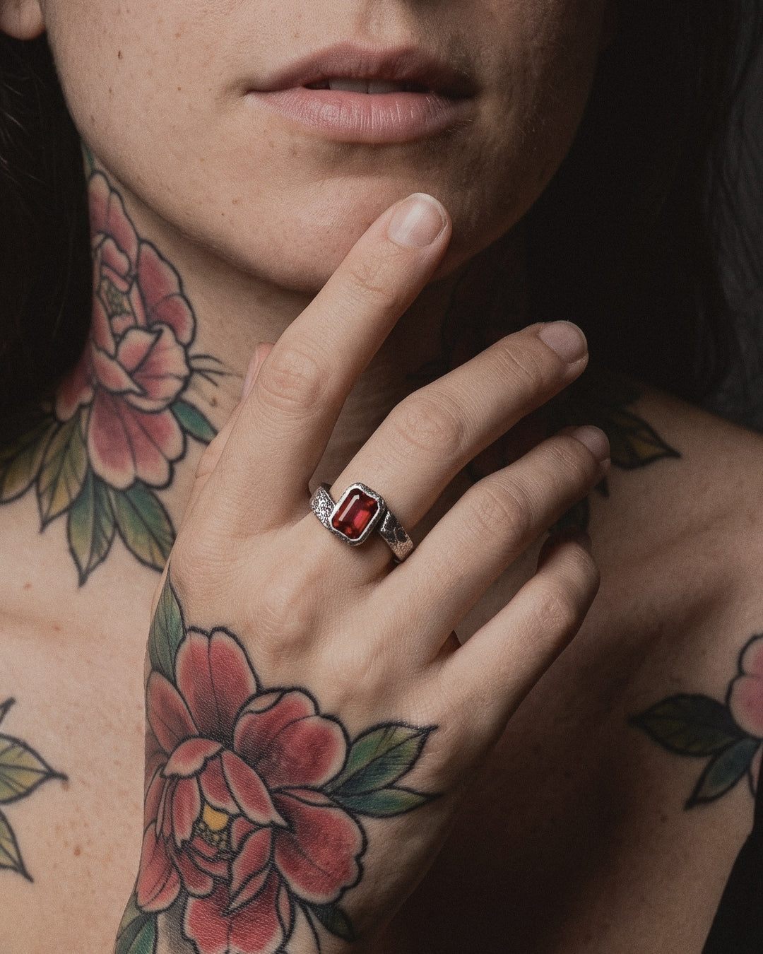 Raw X Ring worn by a woman, her hand at her chin, neo traditional peony tattoos on her neck, chest and arm