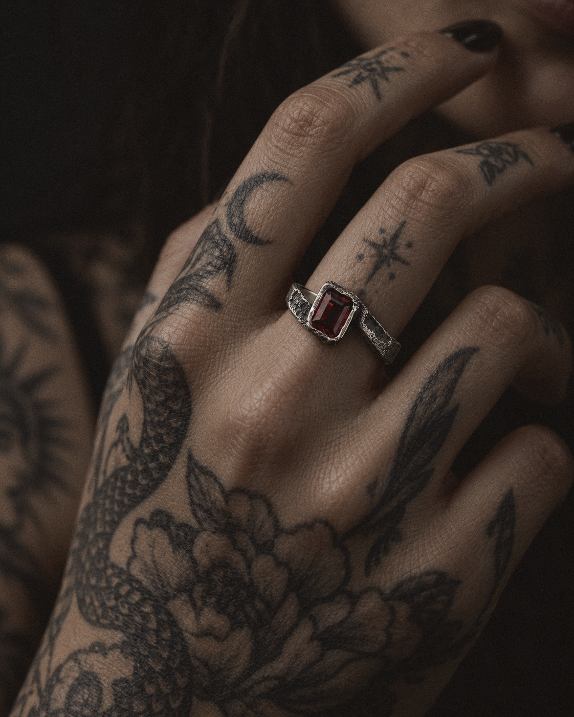 Raw X Ring worn on a woman's tattooed hand with dark nail polish
