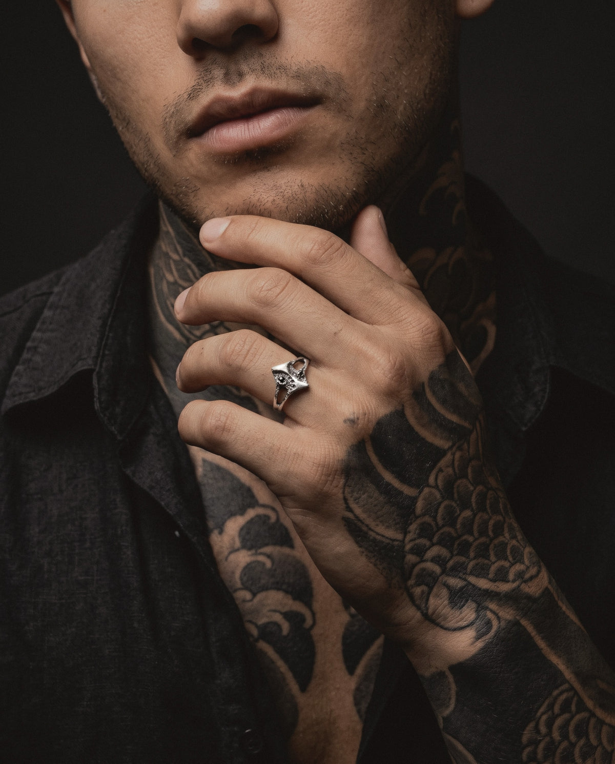 Raw XIX Ring worn by a man, his hand at his chin, Japanese style tattoos on his neck and hand