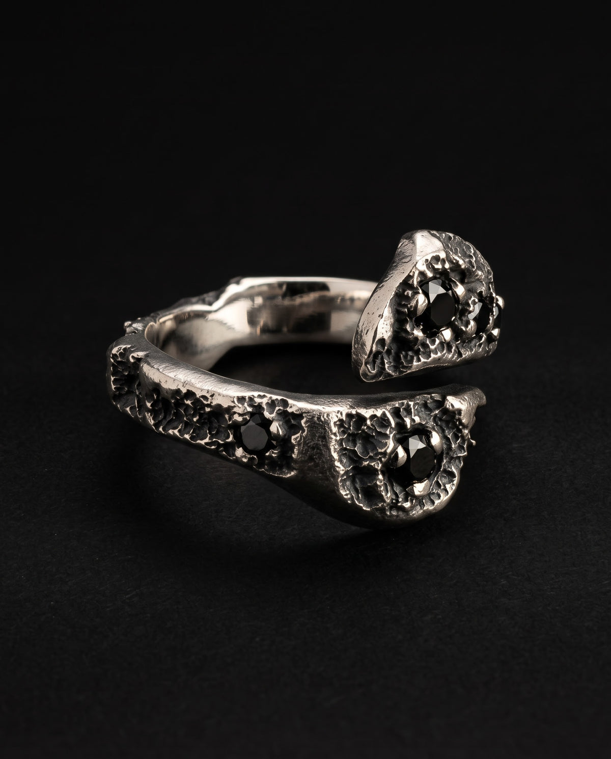 Raw XVII Ring at an angle, the two cratered heads with black stones passing each other, mirror-polished inside