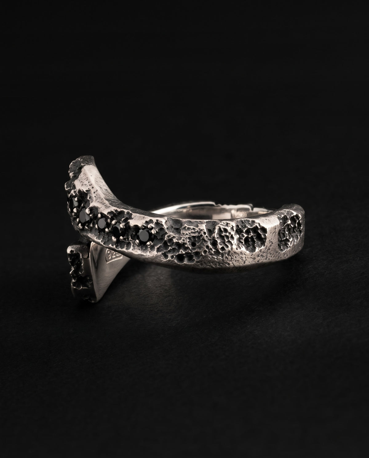 Raw XVII Ring in profile from the other side, black stones along the cratered head and the open band