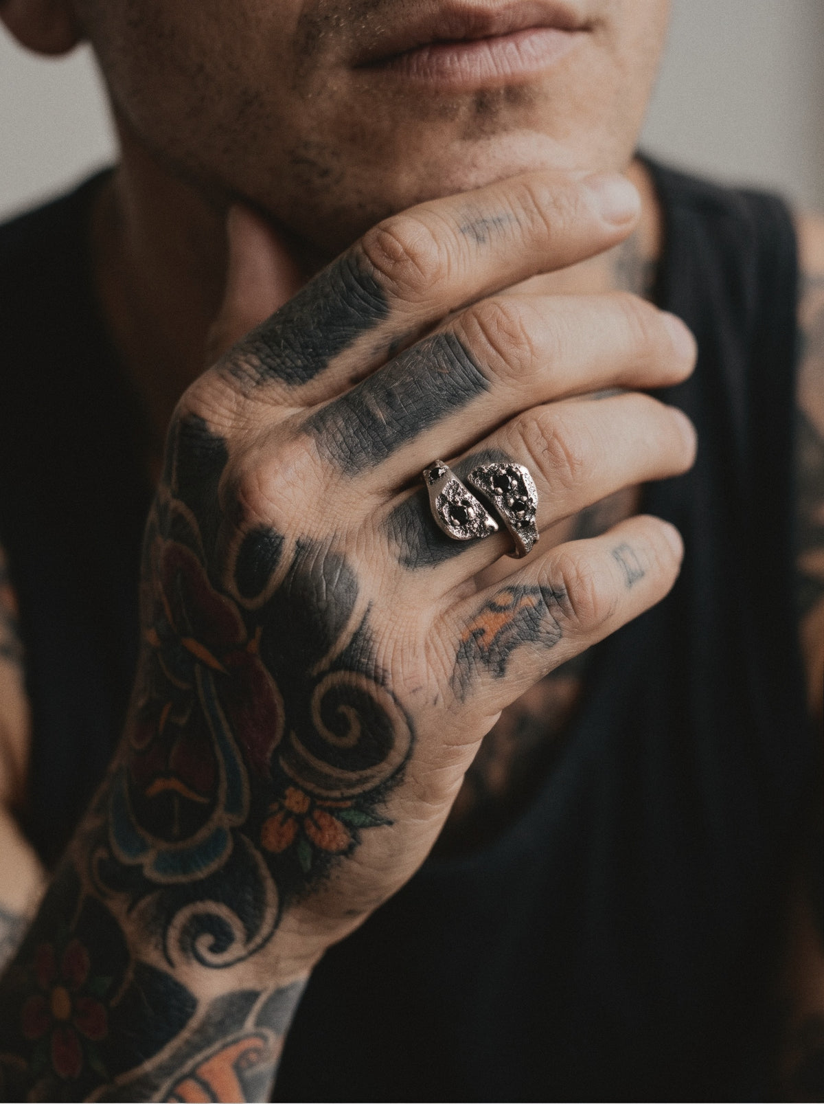 Raw XVII Ring worn on a man's tattooed hand resting at his chin, the two cratered heads with black stones