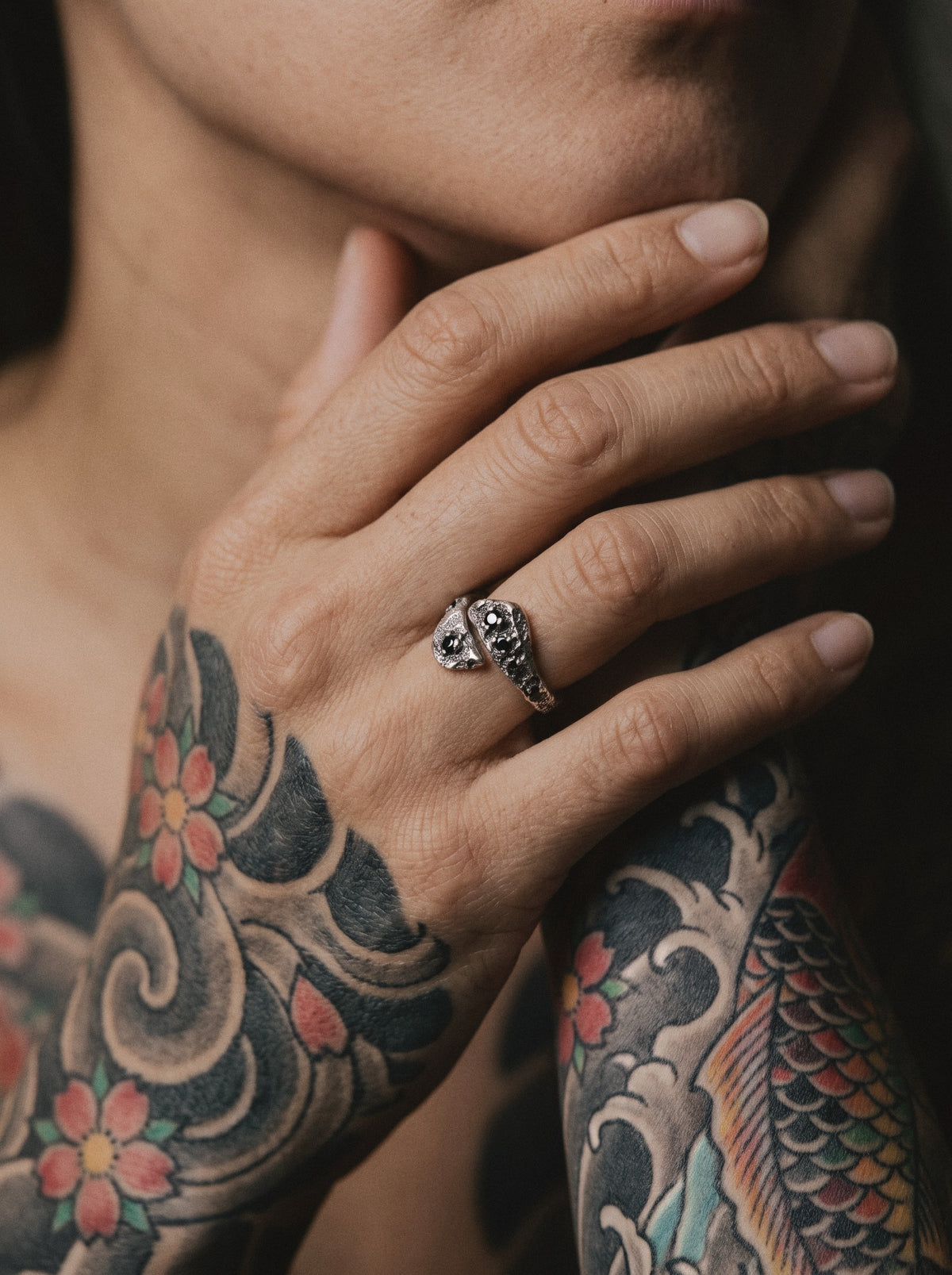 Raw XVII Ring worn on a woman's hand at her neck, her arms covered in Japanese tattoos
