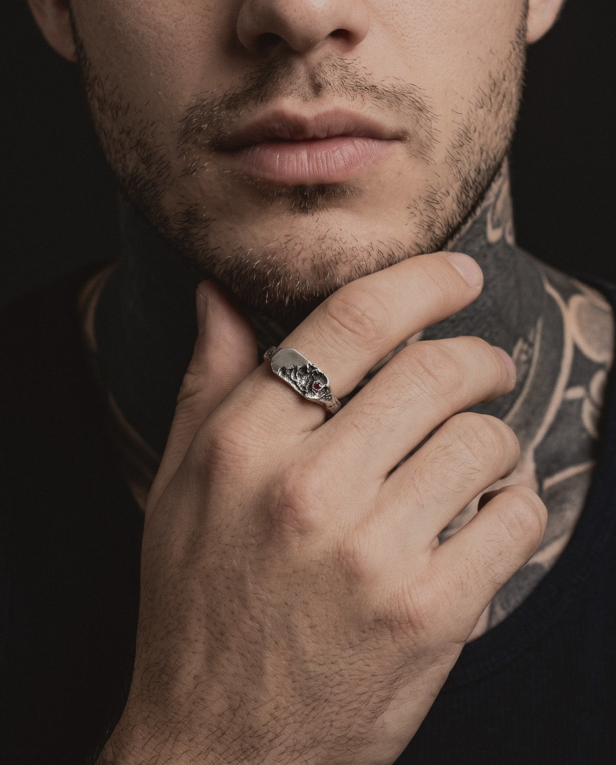 Raw XVIII Ring worn by a bearded man, his hand at his chin, blackwork tattoos on his neck