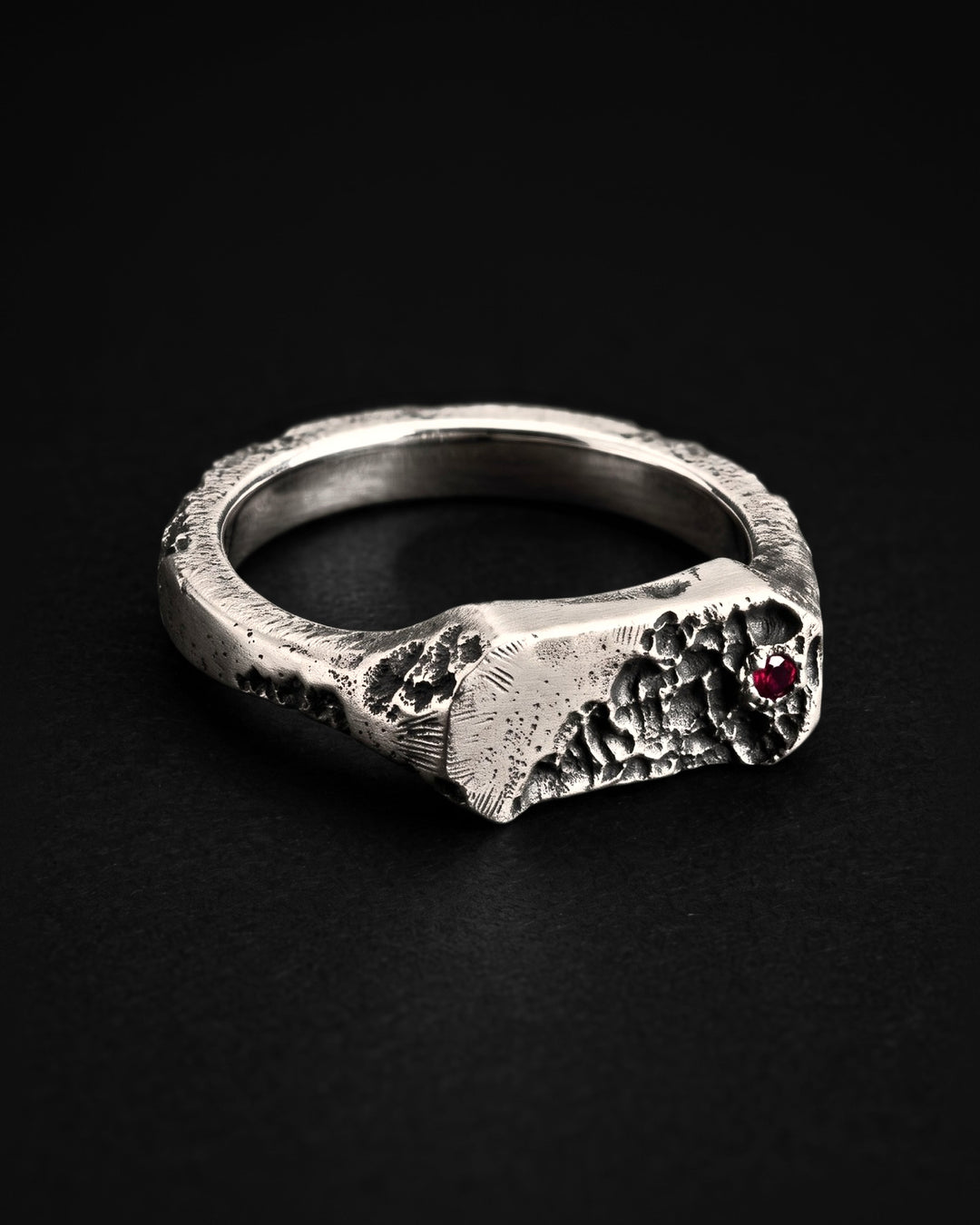 Raw XVIII Ring lying on its side, the cratered end of the face and the red stone